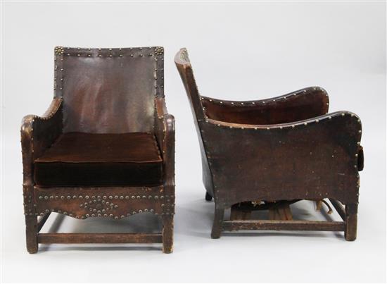 A pair of early 20th century oak framed brown leather and brass studded armchairs,